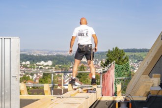 A construction worker on a roof with a view of the urban landscape under bright sky, carpentry, new