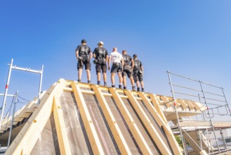 A group of construction workers standing on a roof structure under a blue sky, carpentry, new