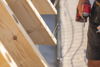 Worker holding drill next to wooden board with screws already screwed in, carpentry, new building,