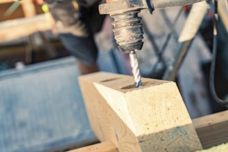 Detailed view of a drill drilling a hole in wood on a construction site, carpentry, new building,