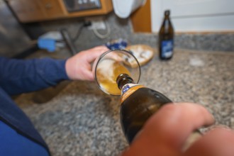 Person pours beer into a glass, the kitchen-like environment makes for conviviality
