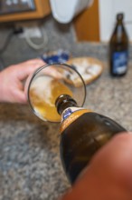 Beer is poured into a glass, and the kitchen as a backdrop creates a relaxed atmosphere