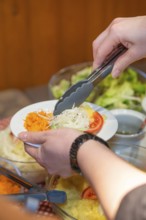 Person serves fresh raw food with tongs on a plate at a buffet