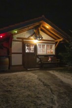 Small wooden hut decorated at night with festive lights and winter accessories