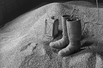 Old stable lantern and felt boots on the grain floor, on a former Franconian farm, black and white,
