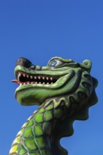 Green dragon with big teeth and long red tongue against blue sky background, Fun Show traveling
