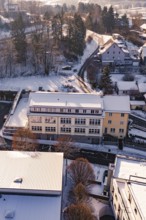 Modern buildings with surrounding roads in a snowy village and wooded area, Nagold, Calw district,
