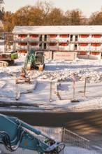 Construction work in front of a snowy building with excavator and equipment in the foreground,