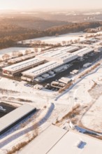Warehouse with surrounding trucks in snow-covered landscape at morning sun, Nagold, Calw district,