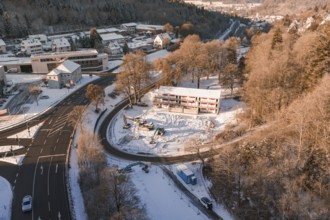 Snow-covered construction site and roads with a view of a wintry settlement and forest, Nagold,