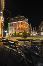 Evening scene with illuminated historic building and empty café chairs in the foreground, Nagold,