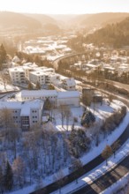 Residential building in a snowy urban landscape with roads and a bridge, surrounded by hills,