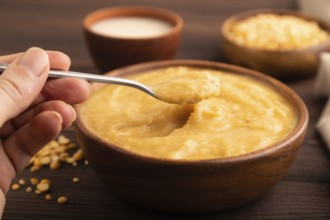 Pea cream soup, Puree, porridge in wooden bowl with hand on wooden background and linen textile.