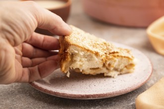 Apple Charlotte cake with hand on brown concrete background and orange linen textile, cup of milk,