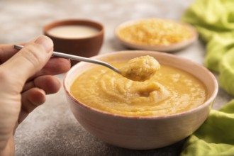 Pea cream soup, Puree, porridge in ceramic bowl with hand on brown concrete background and green