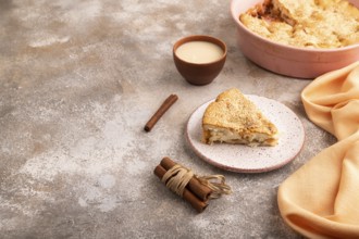 Apple Charlotte cake on brown concrete background and orange linen textile, cup of milk, side view,