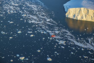 Aerial view of a tourist ship navigating through the fjord among icebergs calved from the
