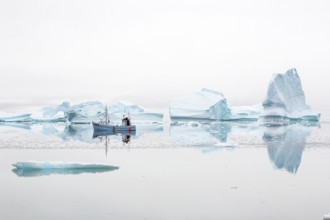Fisherman's boat navigating near floating icebergs in the bay by Ataa village at sunset, Disko Bay,