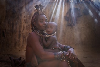 Ovahimba or Himba woman with a baby inside traditional hut, Kaokoland, Kunene Region, Namibia