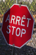 Close-up of bright red bilingual French arret and English stop sign with wire mesh fence in