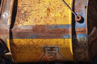 Close-up of discarded old rusted yellow and blue Irving Oil gas container laying on its side