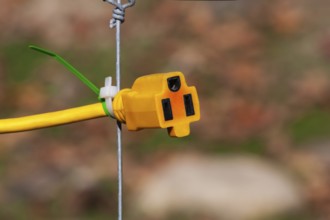 Close-up of yellow female rubber connector power plug attached to wire mesh fence with plastic tie