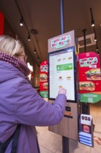 A woman uses an ordering machine in a modern burger restaurant, London, England, Great Britain
