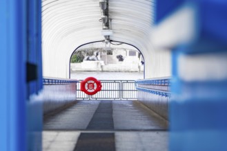 A modern passageway leads to a river, accented with a blue lifebuoy, London, England, Great Britain