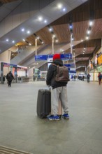 A person in a train station with luggage, modern interior and signpost in the background, London,