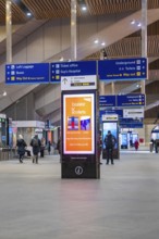Lively train station with signs and people, modern decor and displays, London, England, Great