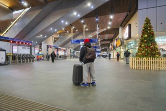 A traveler in a train station with luggage surrounded by modern architecture and Christmas