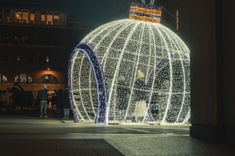 Large illuminated Christmas ball in public square with passers-by at night, London, England, Great