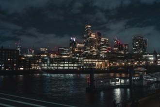 Illuminated skyline of a city at night over a river surrounded by skyscrapers and bridges, London,