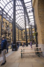 Interior with beer benches and people surrounded by vaulted brick walls and a glass roof, London,