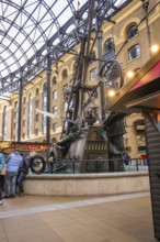 A large metal sculpture in a covered interior surrounded by people, The Navigators, London, United