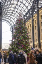 Large decorated Christmas tree in a lively interior with people taking pictures, London, United