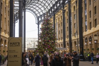 Christmassy decorated gallery with large Christmas tree surrounded by shops and people, London,