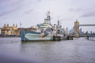 Large historic ship on the river in front of a bridge, with city skyline and towers on the horizon,
