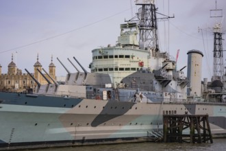 Detailed view of a historic warship with guns, towers in the background, HMS Belfast, London,