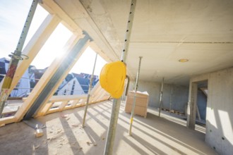 Construction site with yellow helmet on support, light concrete walls and wooden frame, carpentry,