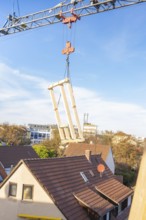 Close-up of a construction crane lifting wooden elements over roofs, carpentry, renovation, roof