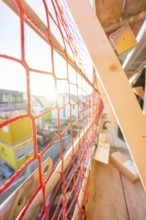 Red safety net on a railing allows sunlight to fall into a construction site, carpentry