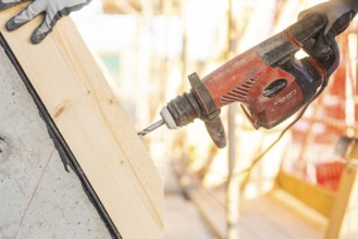 A construction worker uses a drill on an inclined piece of wood on a construction site, carpentry