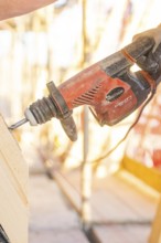 A construction worker operates a red drill on a construction site. Sunlight illuminates the scene,