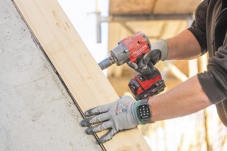 A worker with a cordless screwdriver fixing a piece of wood on a construction site, carpentry