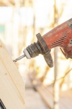 A drill drills into a slanted piece of wood, illuminated by sunlight, carpentry construction, roof