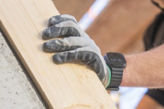 Close-up of a gloved hand holding a wooden plank, carpentry construction, roof extension,