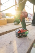 A cordless screwdriver is lying on wooden scaffolding, illuminated by the evening sun, carpentry