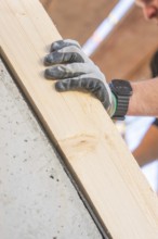 A gloved hand with a smartwatch holds a wooden board at a building, carpentry construction site,