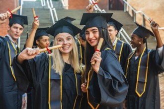 Smiling university graduates of different ethnicities wearing academic gowns and caps, cheering